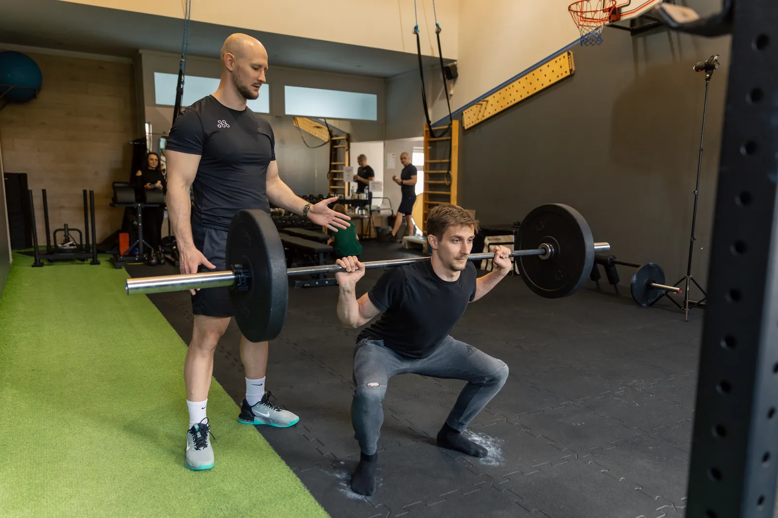 Trener asekuruje przysiad ze sztangą na siłowni Move Center